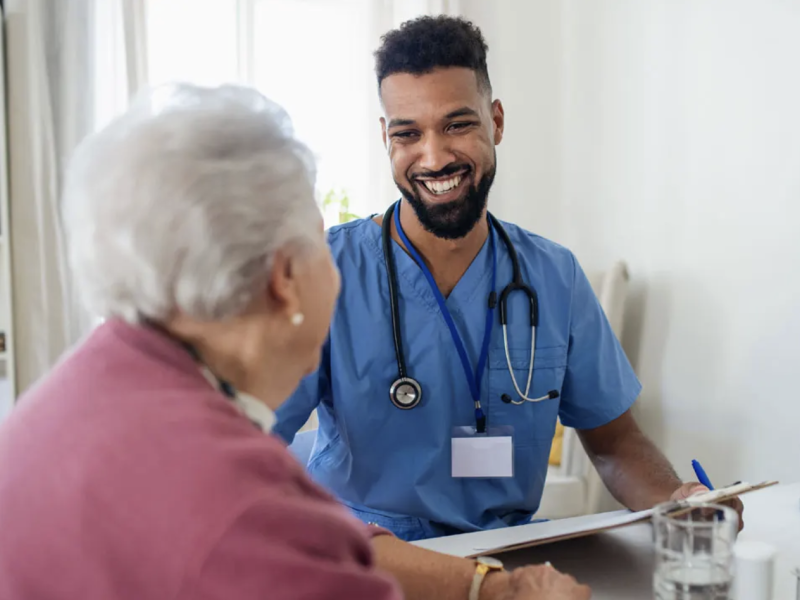Smiling male healthcare worker consults with an elderly woman.