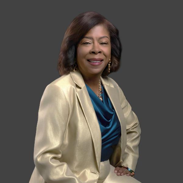 Smiling Black woman in a gold suit jacket and teal blouse.