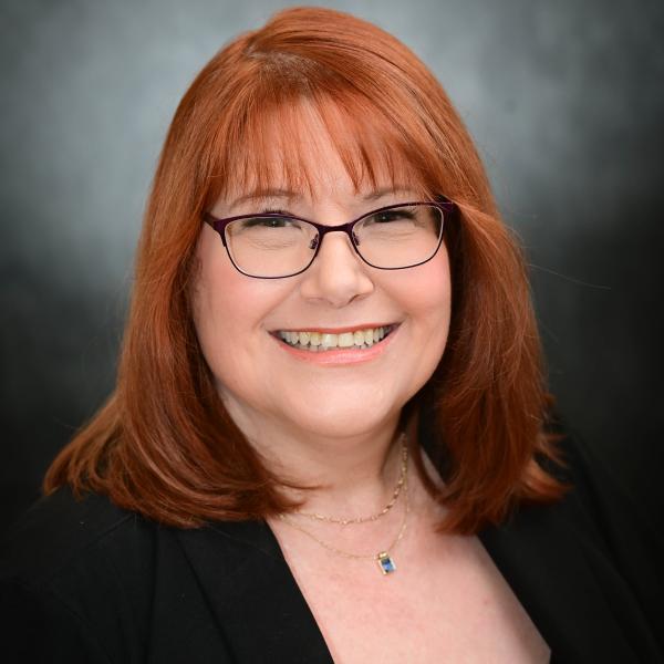 Smiling woman with red hair and glasses in a professional headshot.